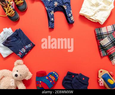 Abbigliamento bambino ragazzo, concetto di doccia bambino. Abiti caldi invernali e giocattoli per un bambino piccolo su sfondo di colore arancione, vista dall'alto, spazio copia Foto Stock