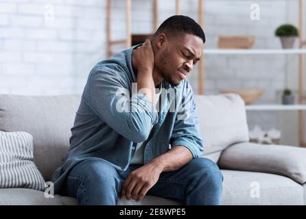 Uomo nero che soffre di dolore al collo seduto sul divano interno Foto Stock