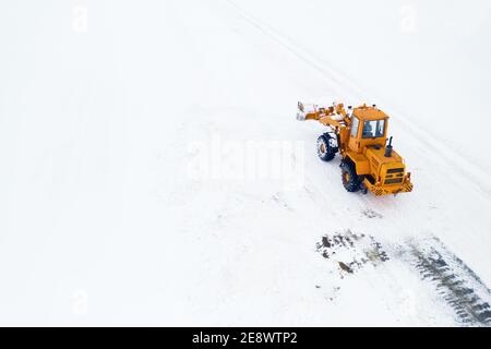 Il trattore giallo con benna rimuove la neve dalla vista dall'alto. Foto Stock