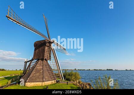 Antico mulino a vento in legno lungo un lago nella provincia olandese Di Frisia Foto Stock