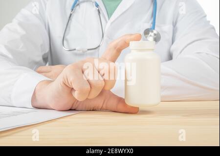 Bottiglia di pillole nelle mani del medico primo piano. Il medico prescrive la medicina al paziente. Medico che prescrive la medicina seduto alla scrivania in off Foto Stock