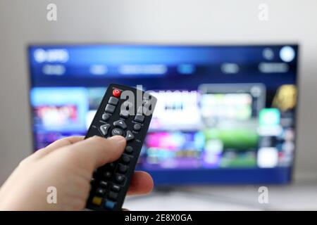 Mano maschile con telecomando sullo sfondo dello schermo Smart TV. Persona che sceglie i servizi di streaming, guardando i film Foto Stock