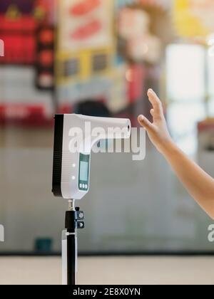 Cliente con maschera protettiva sollevata mano al termometro digitale con macchina per la scansione della temperatura per la febbre prima di entrare nell'area. Screening per preven Foto Stock