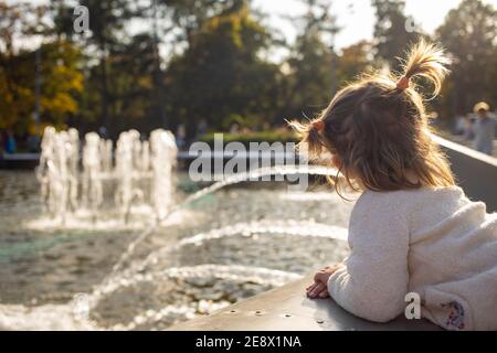 adorabile bambina guarda le fontane nel parco nel parco in una giornata di sole Foto Stock