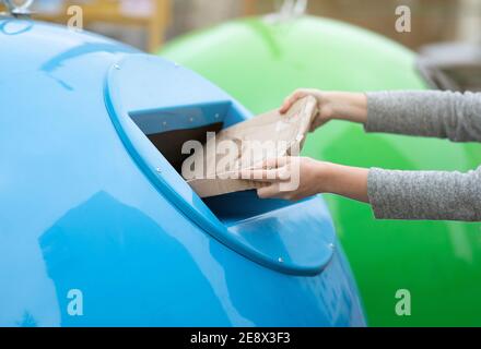 Smistamento Paperwaste. Donna irriconoscibile che lancia la confezione di cartone nel cestino blu per la raccolta dei rifiuti Foto Stock