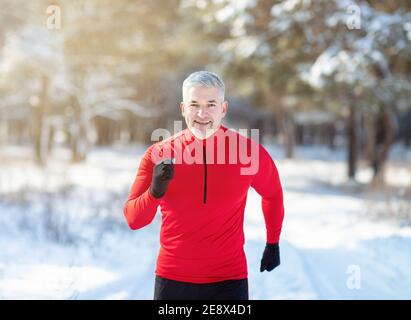 Sci di fondo in inverno. Happy fit uomo anziano jogging nella foresta innevata al mattino soleggiato Foto Stock