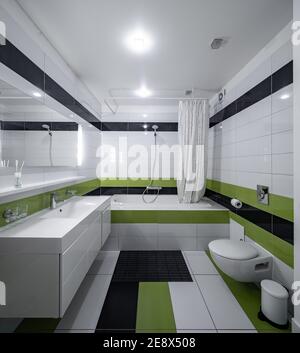 Interni moderni del bagno in un appartamento di lusso. Piastrella bianca, verde e nera. Lavandino e specchio. WC e bagno. Foto Stock