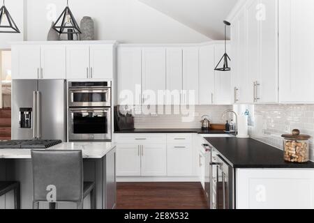 Una bella cucina con una grande isola blu con sgabelli da bar, luci a  sospensione nere, cappa di stufa di design, e armadi bianchi Foto stock -  Alamy