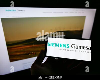 Persona che detiene il cellulare con il logo della società di ingegneria eolica Siemens Gamesa Renewable Energy S.A. in esposizione. Mettere a fuoco sullo schermo del cellulare. Foto Stock
