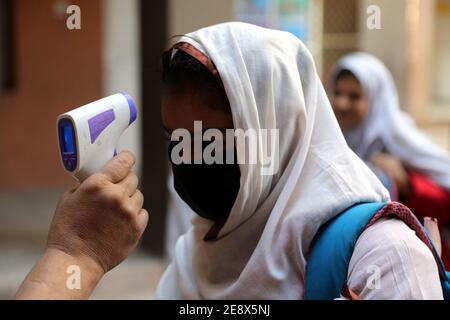 I funzionari della scuola controllano la temperatura corporea degli studenti e sanitizzando le mani prima di entrare a scuola come misura preventiva contro la diffusione del coronavirus (COVID-19), a Peshawar lunedì 01 febbraio 2021. Le scuole primarie e medie e le università in tutto il Pakistan hanno riaperto oggi (lunedì) dopo un intervallo di quasi tre mesi mentre il paese continua a combattere la seconda ondata della pandemia del coronavirus. Foto Stock