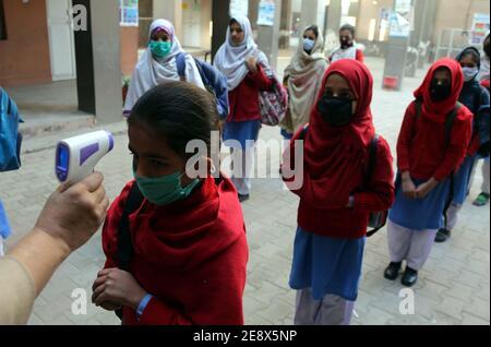 I funzionari della scuola controllano la temperatura corporea degli studenti e sanitizzando le mani prima di entrare a scuola come misura preventiva contro la diffusione del coronavirus (COVID-19), a Peshawar lunedì 01 febbraio 2021. Le scuole primarie e medie e le università in tutto il Pakistan hanno riaperto oggi (lunedì) dopo un intervallo di quasi tre mesi mentre il paese continua a combattere la seconda ondata della pandemia del coronavirus. Foto Stock