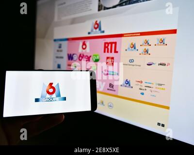 Persona che detiene il cellulare con il logo della società francese di media holding Metropole Télévision S.A. (Groupe M6) in esposizione. Mettere a fuoco sullo schermo del cellulare. Foto Stock