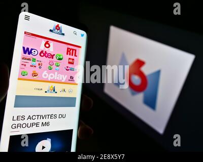 Persona che detiene il cellulare con il sito web della società di media francese Metropole Télévision S.A. (Groupe M6) davanti al logo. Concentrarsi sul centro dello schermo del telefono. Foto Stock