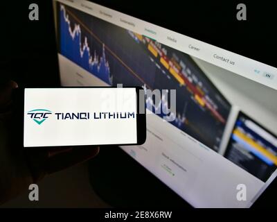 Persona che tiene il cellulare con il logo della società mineraria cinese Tianqi Lithium Corp in esposizione davanti alla pagina web. Mettere a fuoco lo schermo dello smartphone. Foto Stock
