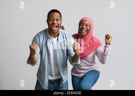 Coppia nera emozionale che celebra il successo, i pugni clenching e gridando Foto Stock