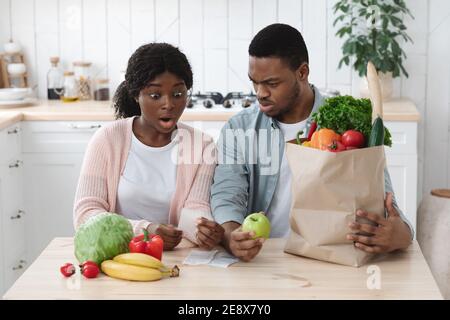 Scossa Coppia nera in cucina che verifica fattura dopo acquisti alimentari Foto Stock