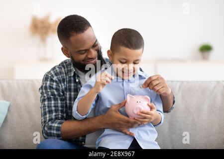 Padre africano e Figlio mettere denaro in Piggybank a casa Foto Stock