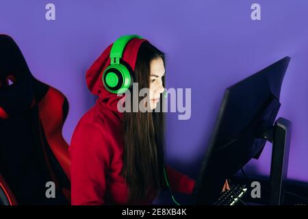 Una giovane ragazza che gioca un gioco per computer su poltrona professionale contro monitor in cuffie verdi, live streaming, eSport. Foto Stock