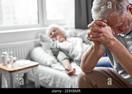 l'uomo anziano piangendo e piangendo per la perdita della moglie, seduto al suo fianco. focus su uomo sconvolto guardando giù. coronavirus, covid-19 concetto Foto Stock