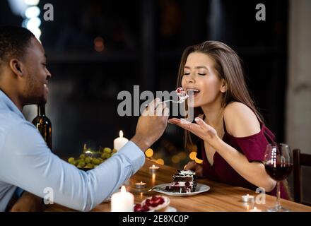 Coppia mista che si nutrire con dessert in data romantica nel ristorante Foto Stock