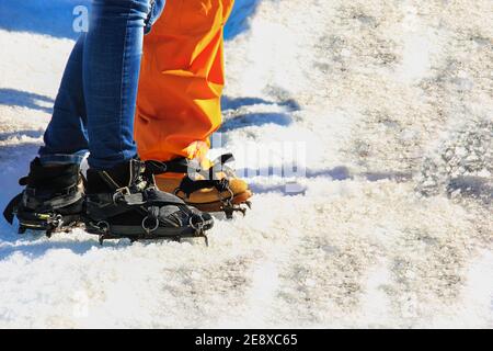 Primo piano delle gambe inferiori di due viaggiatori che iniziano a salire sul ghiacciaio. Piedi di coppia innamorati in scarpe ramponi sul sentiero glaciale. Escursioni romantiche. Foto Stock