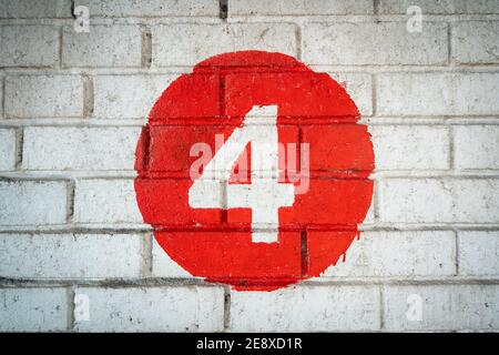 Colore bianco dipinto a mano livello numero quattro al centro di un cerchio rosso dipinto su un vecchio mattone testurizzato parete con le piste nel colore Foto Stock