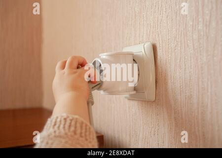 Il bambino gioca con una presa, tira le mani su di esso, le bastone le dita. Il bambino è in pericolo a casa. Le dita del bambino nella presa. Paura Foto Stock