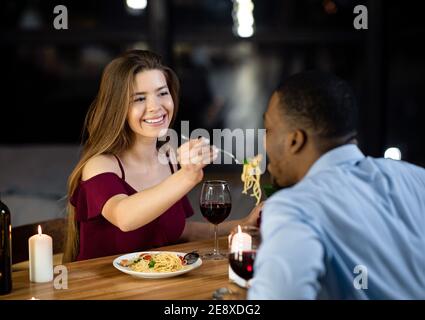 Donna amorevole nutrendo il suo ragazzo Nero con gli Spaghetti durante la cena Nel ristorante Foto Stock