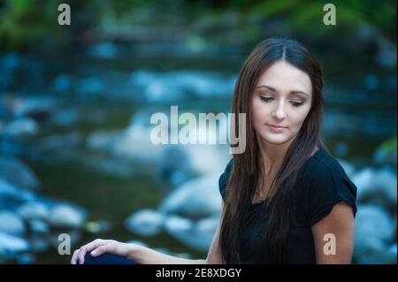 Una giovane donna si pone lungo le rive di un piccolo fiume. Foto Stock