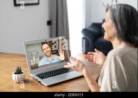 Un ragazzo sullo schermo del computer portatile agitando la mano, salutando con una donna anziana, una studentessa che parla di incontro virtuale con un'anziana tutor femminile, un figlio adulto chiama Foto Stock