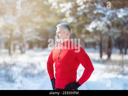 Ragazzo maturo atletico in abbigliamento sportivo che si rompe durante il suo allenamento invernale all'aperto al parco innevato. Concetto sportivo stagionale Foto Stock