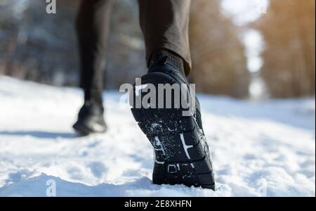 Vista ritagliata dello sportivo che fa jogging su strade innevate in inverno, primo piano dei piedi in scarpe da ginnastica, spazio per le copie. Attività all'aperto Foto Stock