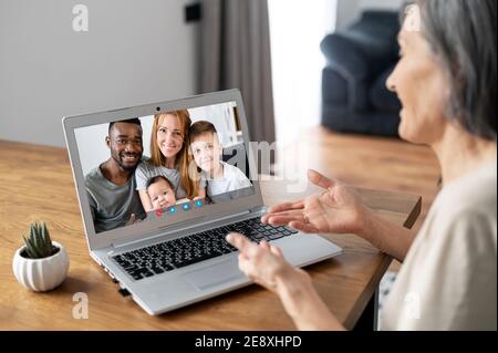 Indietro visualizza una donna anziana che utilizza un computer portatile per videochiamare. Una madre anziana sta parlando in linea con una figlia adulta e la sua famiglia multirazziale, video Foto Stock