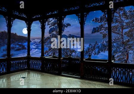 Vista dalla galleria di legno della magica notte invernale in una costa di mare innevata circondata da alberi di abete innevato con luna piena in un cielo stellato. Vista di fo Foto Stock