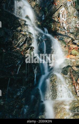 Lunga esposizione cascata cremosa sul piccolo ruscello della foresta dalla neve di scongelamento brillata dal sole del tramonto. repubblica Ceca Foto Stock