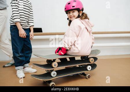 Affascinante ragazza in casco rosa seduta su un triplice skate catasta presso lo skatepark al coperto Foto Stock