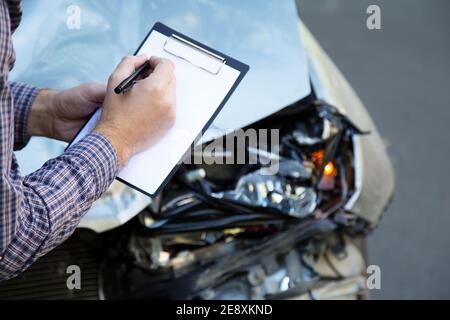 Mani maschili con carta mock su assicurazione auto vuoto contro auto distrutta in auto incidente stradale incidente. Rottura del faro anteriore automatico acceso Foto Stock