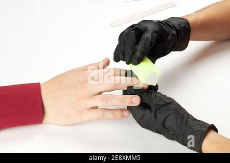 manicurista durante il lavoro con chiodo di bucf. un processo di manicure dell'uomo. una persona caucasica irriconoscibile che fa il servizio di unghie al salone di cure estetiche. Foto Stock