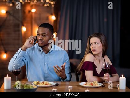 Black Guy che parla su Cellphone a Date mentre la sua ragazza Seduta noiosa Foto Stock