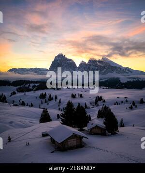 Chalet in legno coperto di neve all'alba con Sassolopiatto e Sassolungo sullo sfondo, Alpe di Siusi, Dolomiti, Alto Adige, Italia Foto Stock