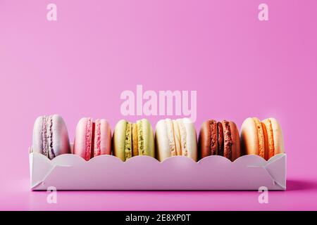 Biscotti colorati di macaron francesi in un pacchetto su sfondo rosa. Primo piano, spazio libero Foto Stock