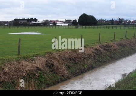 Campo innevato d'acqua e diga dopo forti piogge con edifici agricoli all'orizzonte Foto Stock