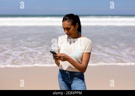Donna afroamericana che usa uno smartphone su una spiaggia vicino al mare Foto Stock