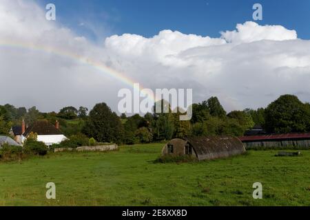 Arcobaleno distante su un campo contadino e cottage bianco in Wiltshire Foto Stock