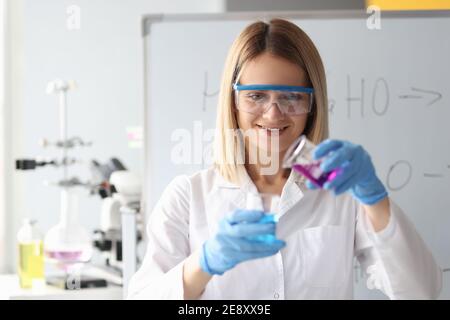 Donna chimico in occhiali protettivi versando liquido dalla beuta Foto Stock