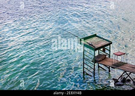 Una canna da pesca poggia su un'alta piattaforma di legno vicino alla riva del fiume. Foto Stock