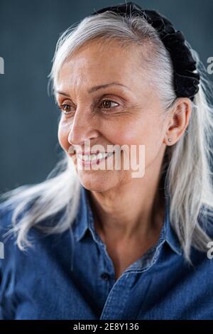 Ritratto di donna anziana in piedi in interni su sfondo scuro. Foto Stock