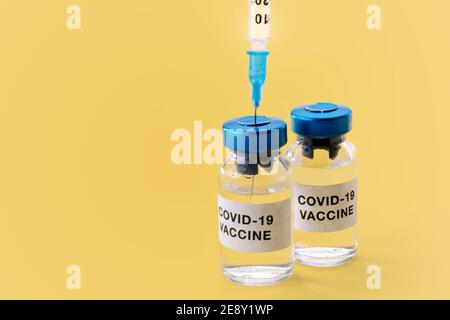 Vaccino COVID-19 del coronavirus. Fiale con siringa isolata su sfondo giallo, composizione concettuale con spazio per la copia Foto Stock