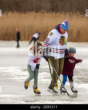 Padre con due giovani figlie che giocano a hockey su ghiaccio su un lago ghiacciato Foto Stock