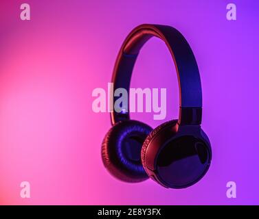 Eleganti cuffie wireless nere illuminate con coloratissima luce al neon su sfondo astratto isolato. Concetto di tecnologia moderna con spazio di copia Foto Stock